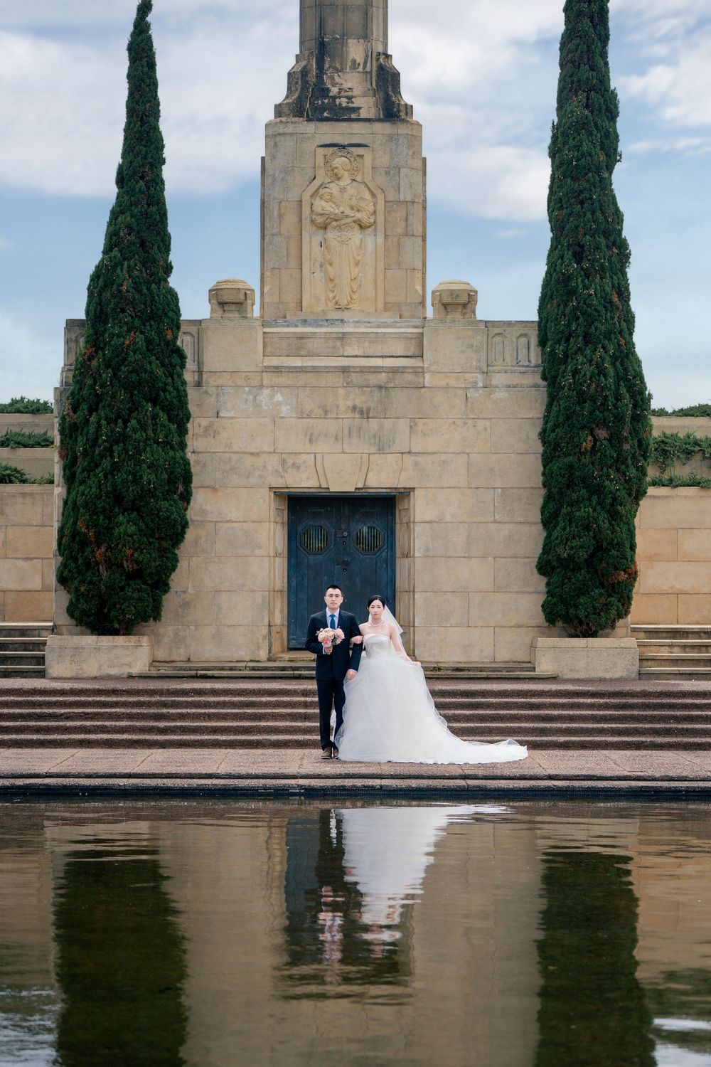 Cinematic wedding photography portrait of a couple standing by the reflection pool in front of the Auckland War Memorial Museum.