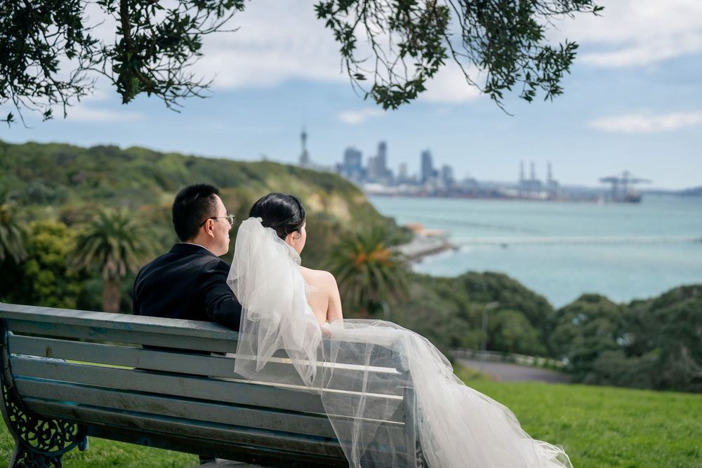 Romantic couple sitting on a park bench looking at the beautiful Auckland city skyline and harbour.