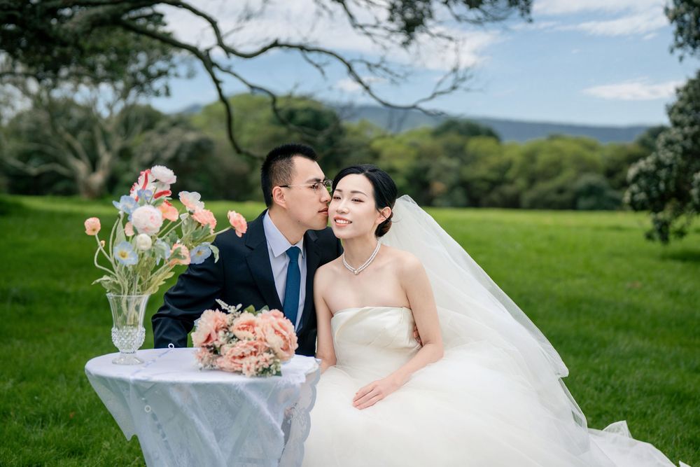 Groom kissing the bride gently at an elegant outdoor floral picnic table.