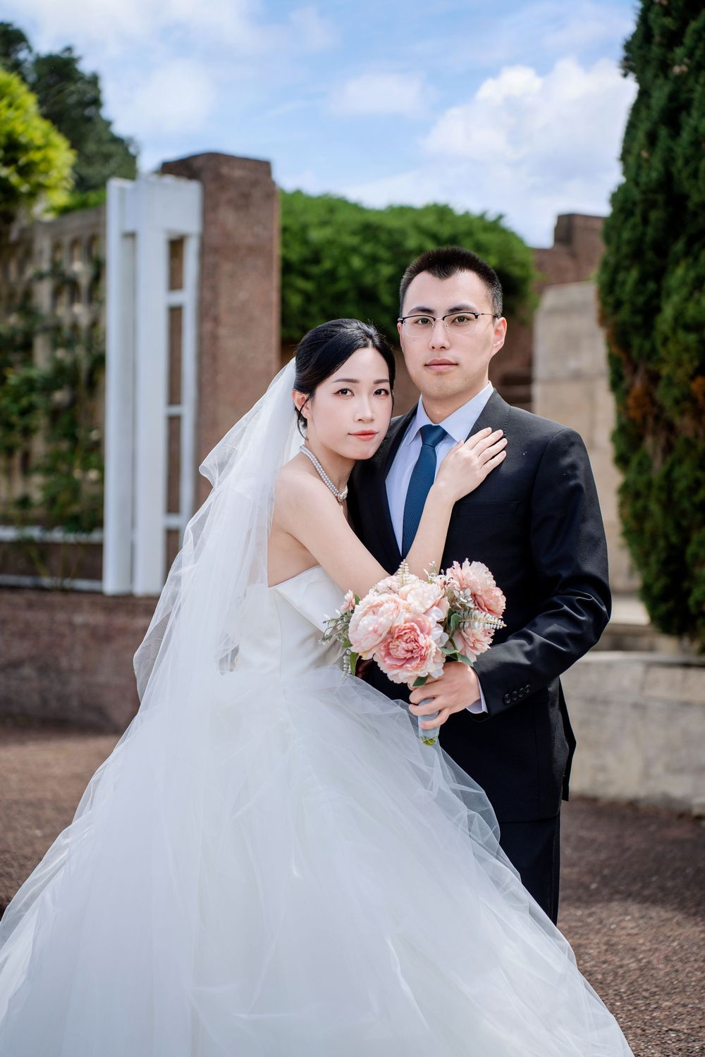 Elegant bride and groom standing together in a beautiful garden pathway for Auckland pre-wedding photos.