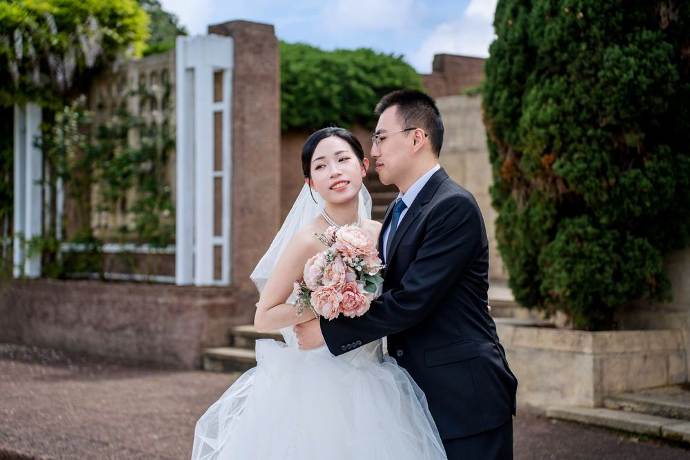 Romantic groom hugging the bride from behind in a lush outdoor garden in New Zealand.