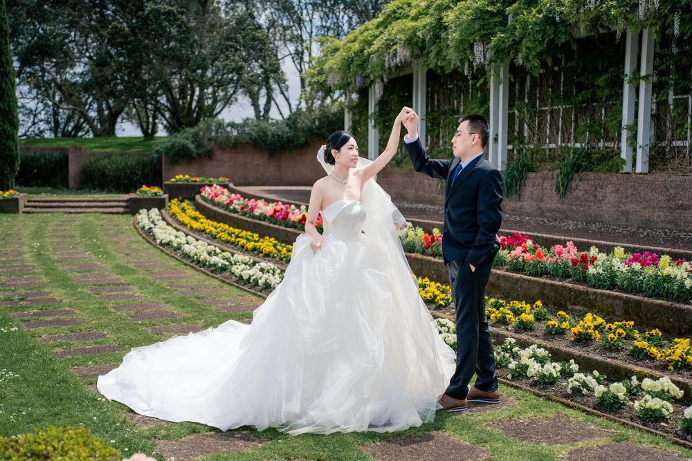 Groom twirling the bride in her beautiful wedding dress in a sunlit formal garden setting.