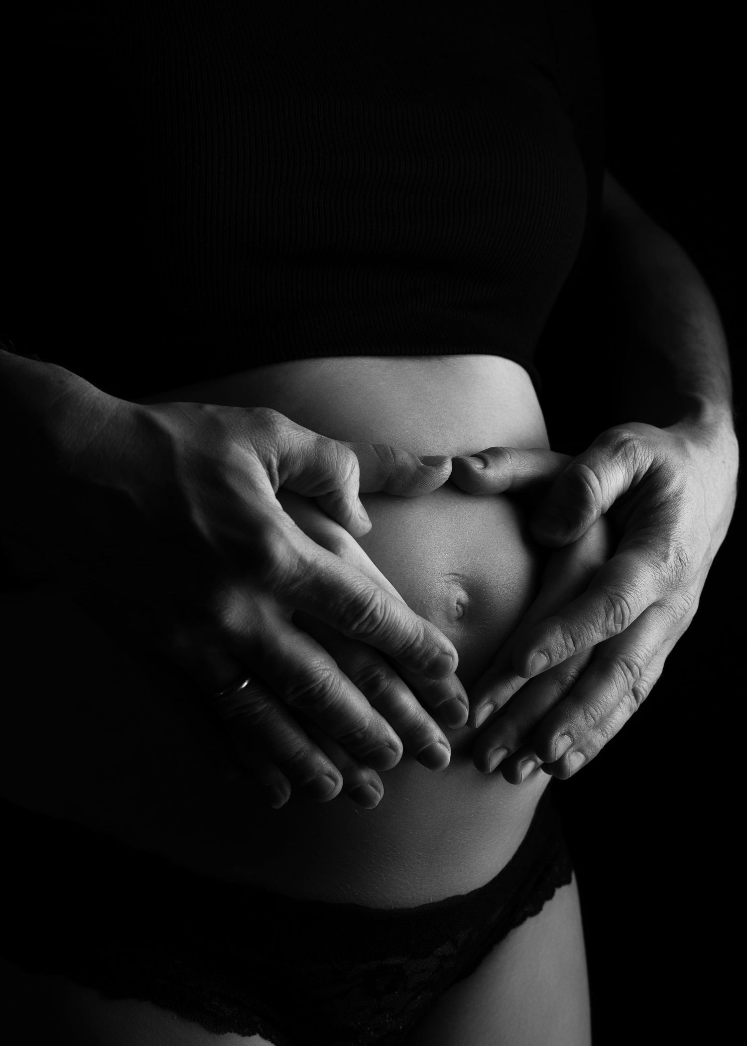 a black and white photo from a maternity photo shoot in studio depicting a couple's hands resting on a baby bump