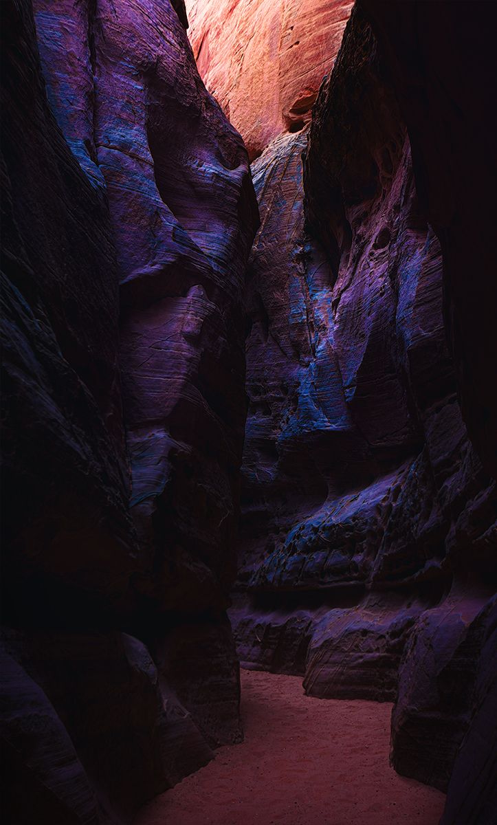 Narrow slot canyon with dramatic purple and red rock walls illuminated by natural light filtering from above.