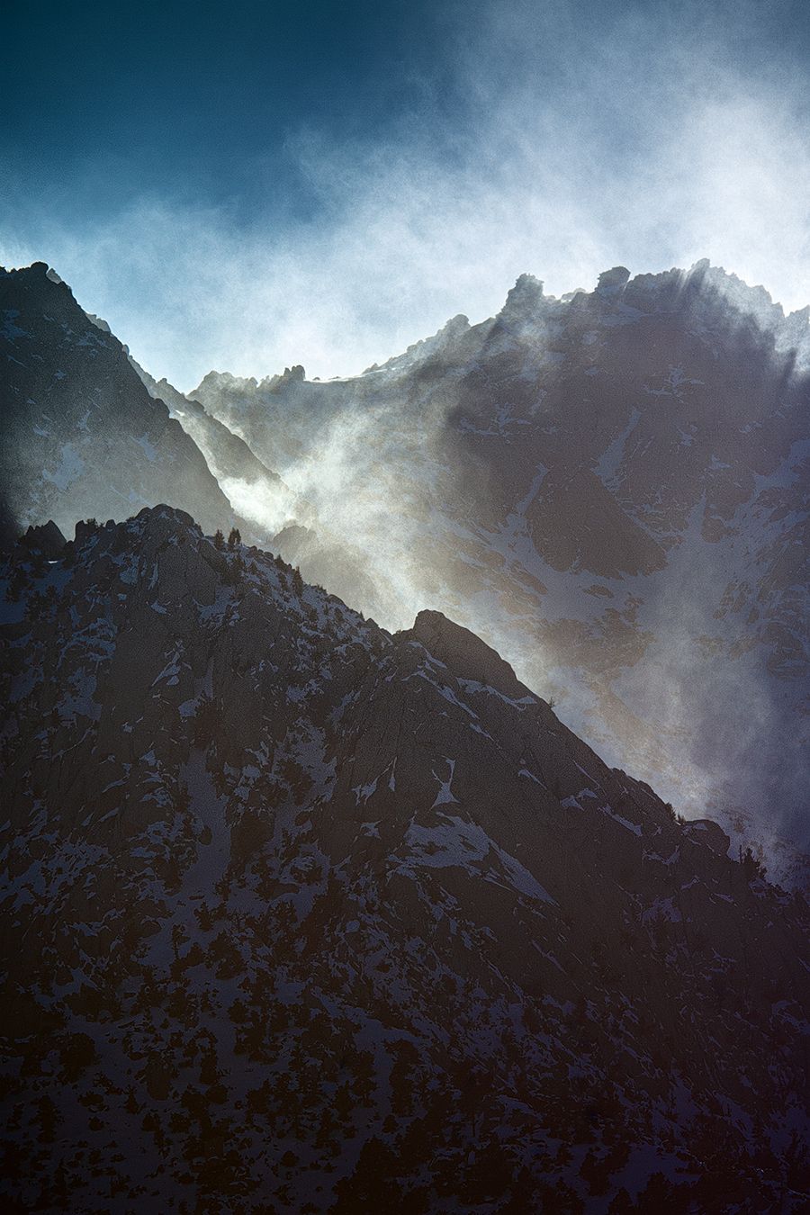 Misty mountain peaks shrouded in dramatic storm clouds with sunlight breaking through.