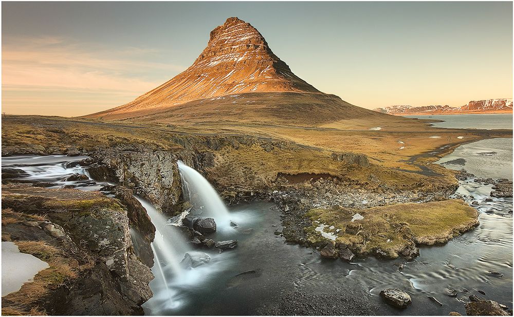 Kirkjufell mountain towers above double waterfalls in scenic Icelandic landscape.