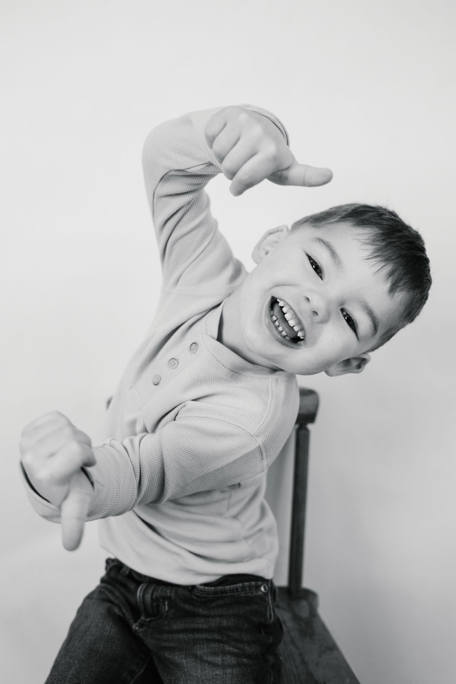 Energetic young boy laughing and striking a fun pose in a black and white studio portrait.