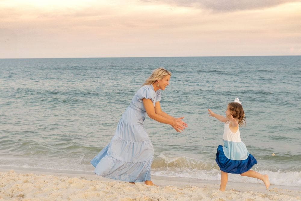 Playful beach scene with two people in blue dresses dancing by the ocean at sunset.