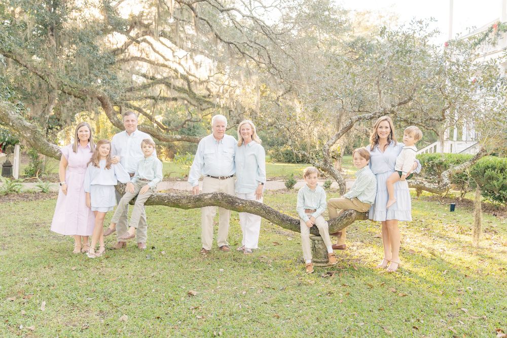 A group in white and beige outfits posing on a fallen tree branch in a sunlit outdoor setting.