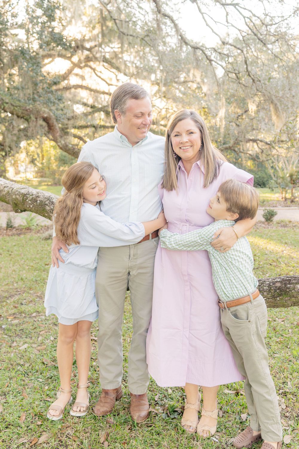 A family of four embracing in an outdoor setting with Spanish moss trees in the background.