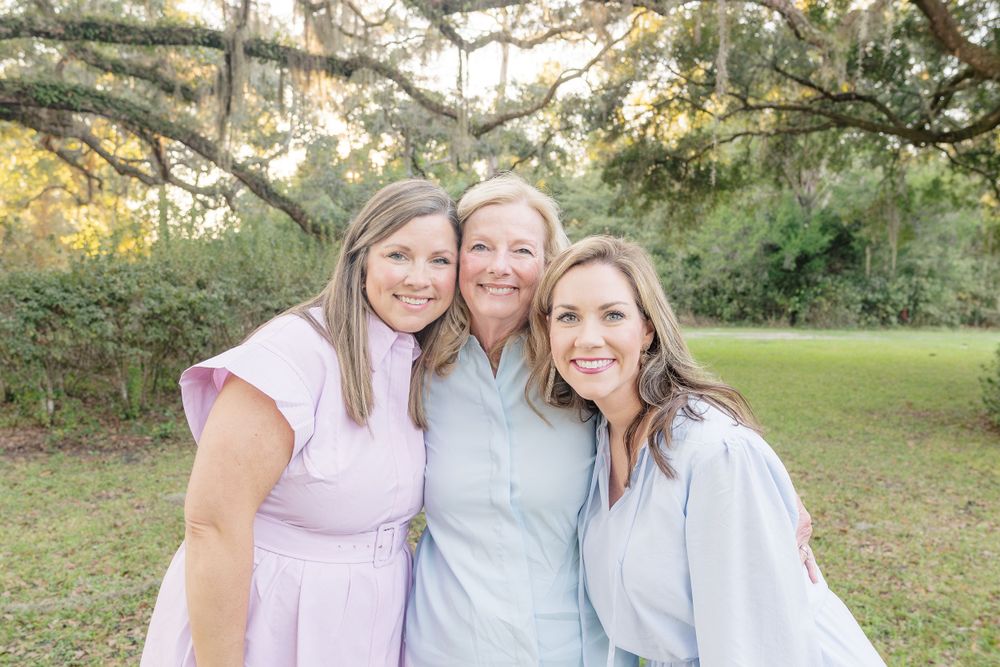 Three people in pastel outfits share a close moment outdoors.