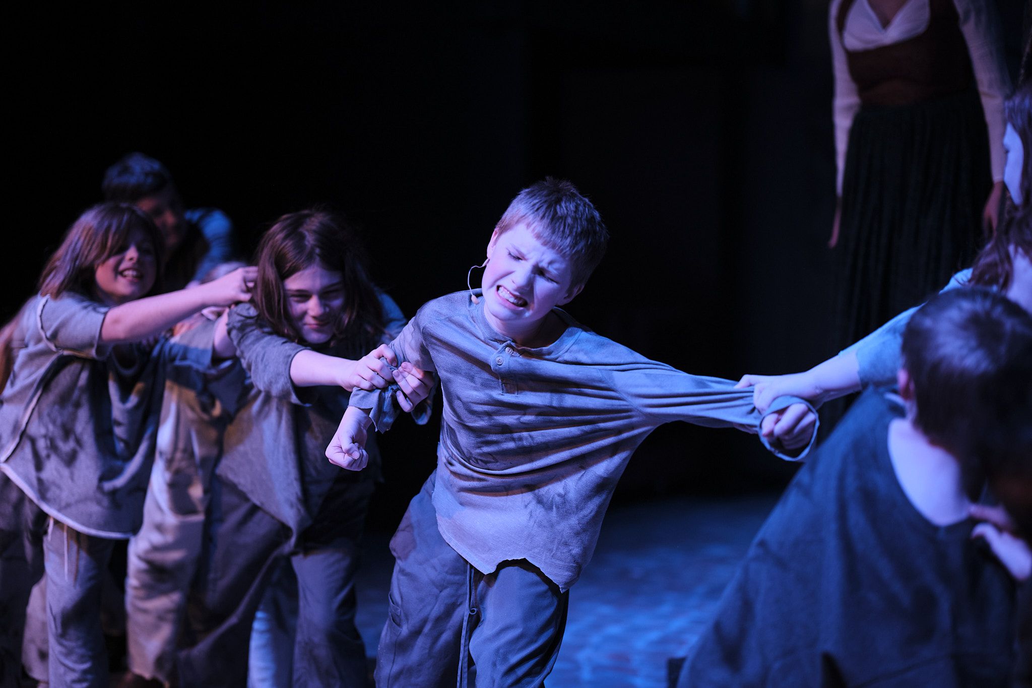 Performers in period clothing create dynamic movement scene under blue stage lighting.