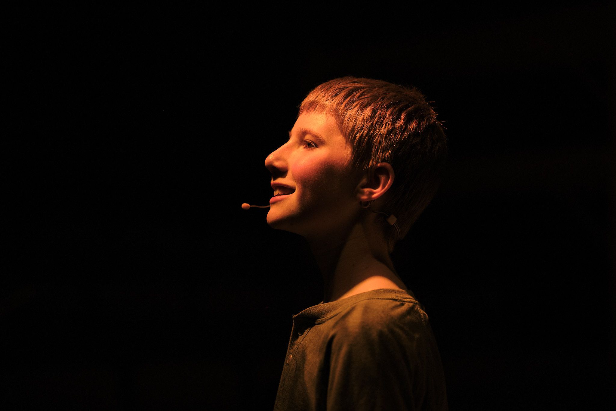 Side profile of performer illuminated dramatically against dark background on stage.