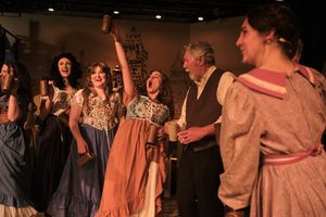 Theater ensemble wearing historical costumes performs together on stage.