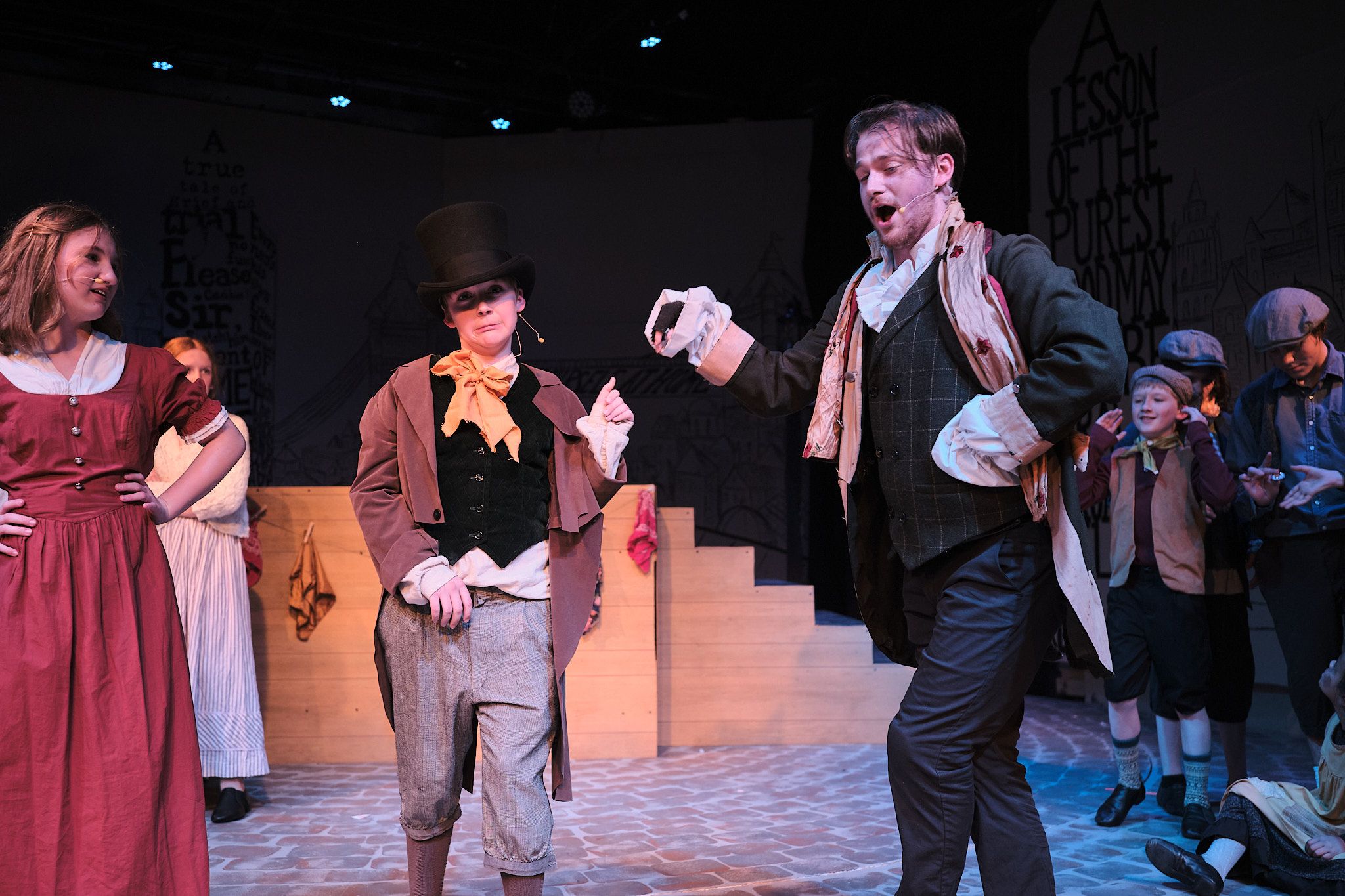 Theatrical scene with actors in period costumes performing on a multi-level stage set.