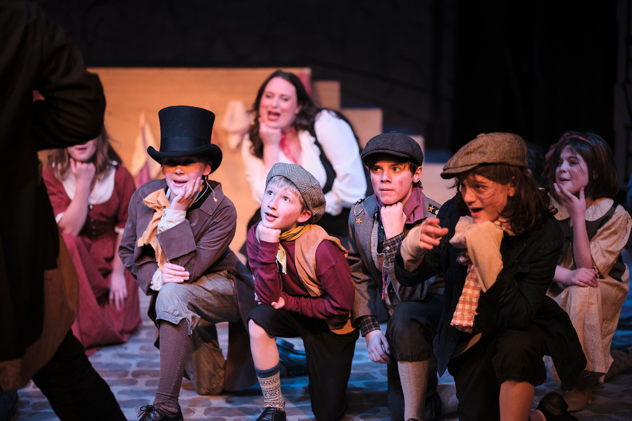 Cast members in Victorian-era costumes performing energetic scene with top hats and historical attire.