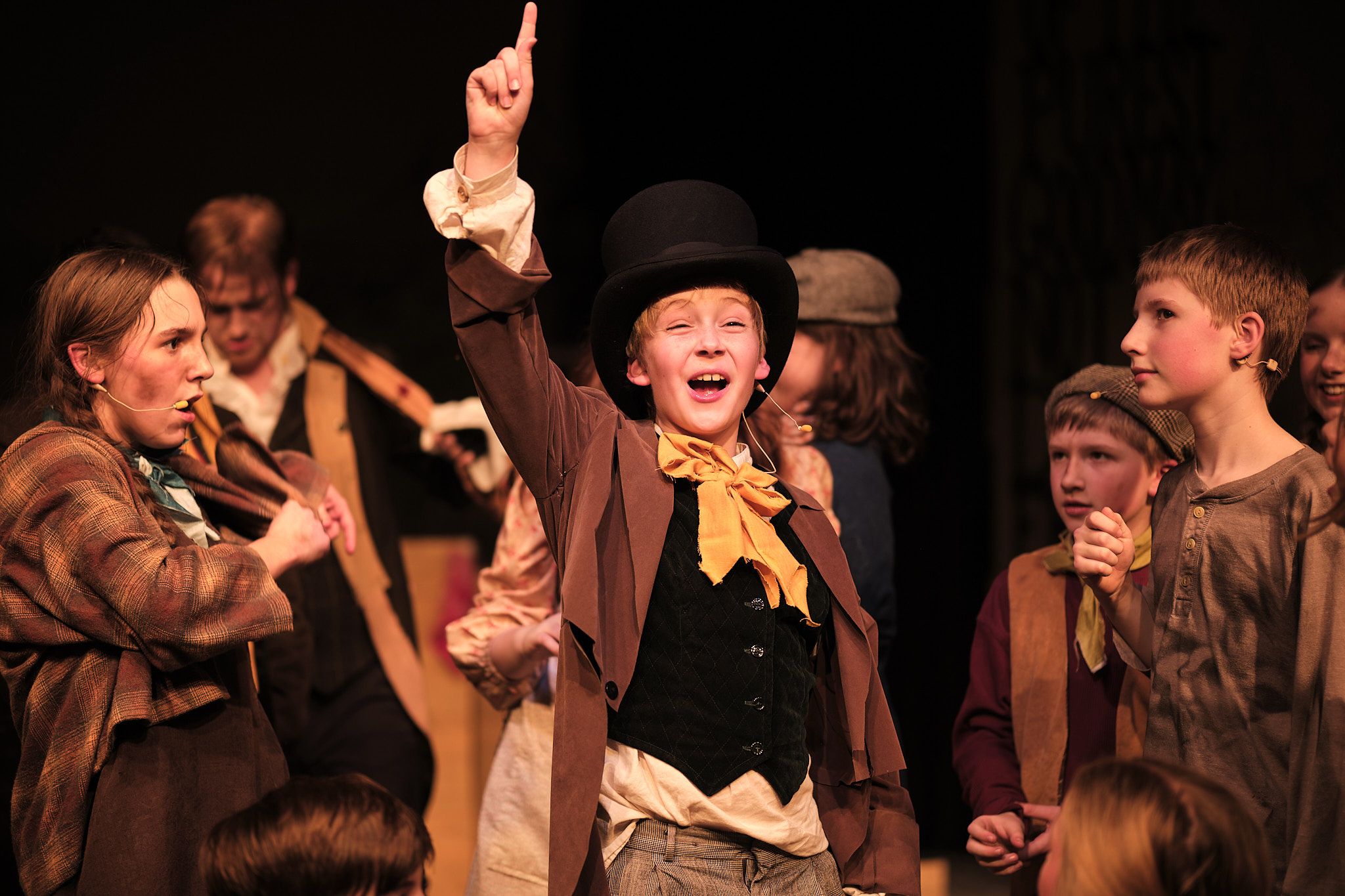 Theater performer in top hat and vest gestures dramatically during stage production.