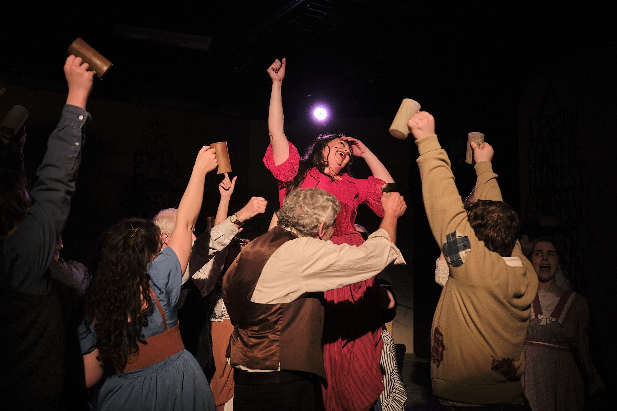 Energetic theatrical scene with performers raising arms in celebration during musical number.