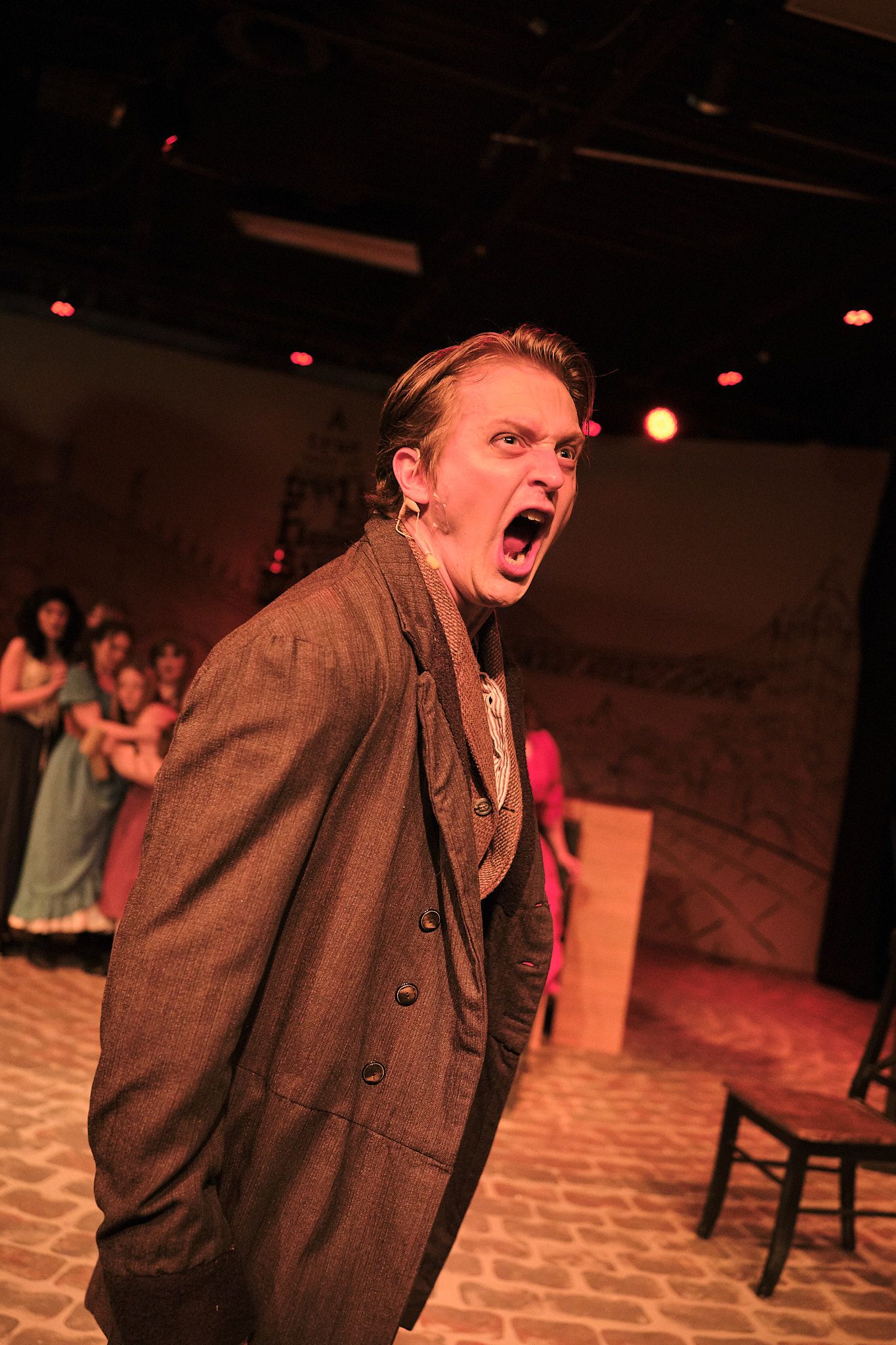 Actor in period costume performs intense dramatic scene under stage lighting.
