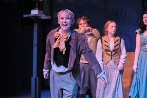 Cast members in Victorian-era costumes perform scene on theatrical stage.