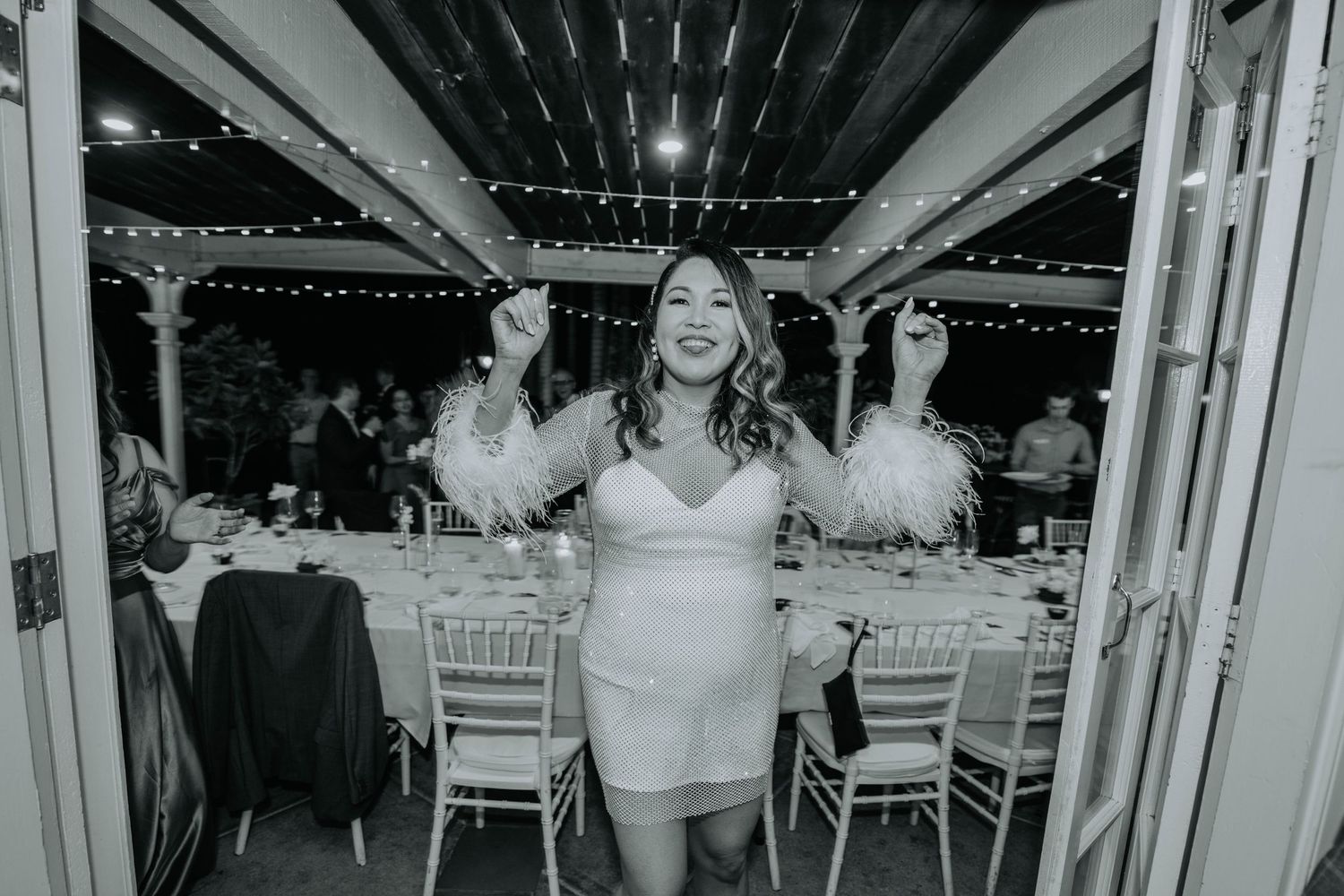 Black and white photo of celebratory moment at a reception with string lights overhead.