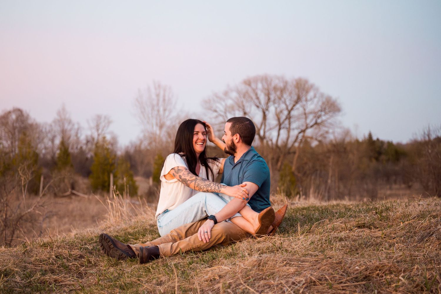 Couple sharing tender moment on grassy hill during sunset.