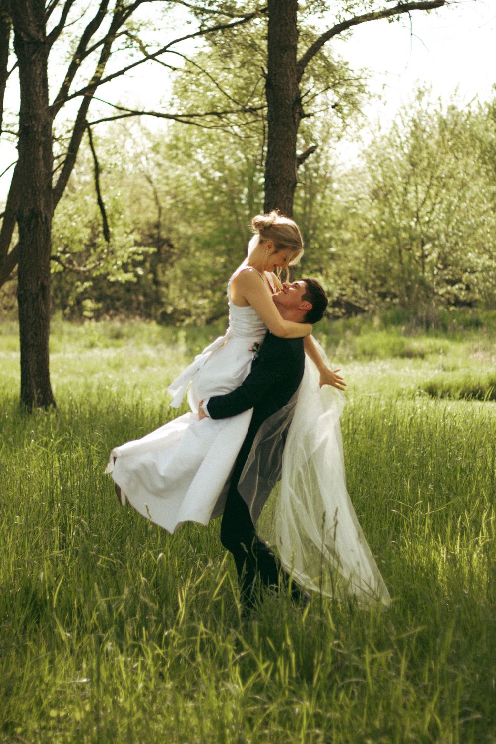 A couple shares a romantic dance lift in a sunlit meadow.