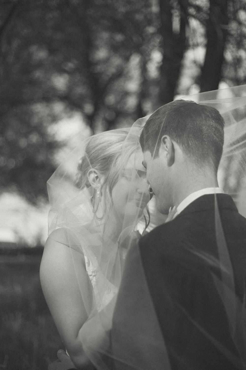 An intimate black and white portrait of a couple sharing a tender moment under a veil.