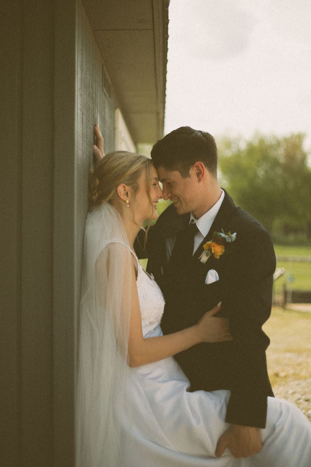 A romantic wedding portrait showing a close embrace against a rustic wall backdrop.