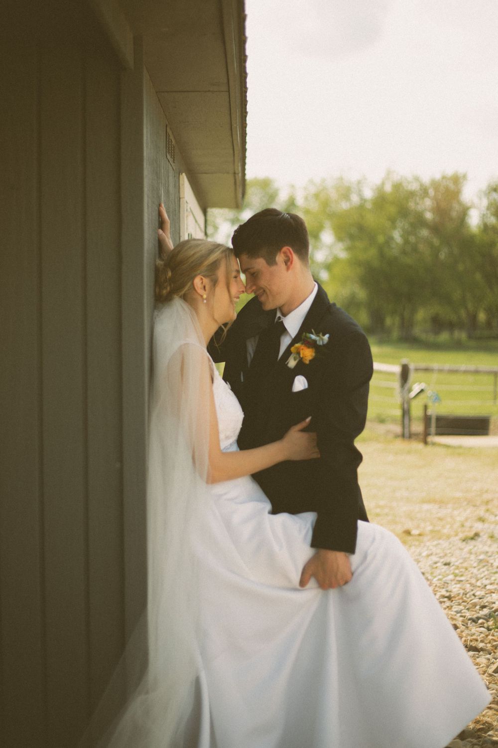 An intimate wedding photo against a building wall showing a tender moment between newlyweds.
