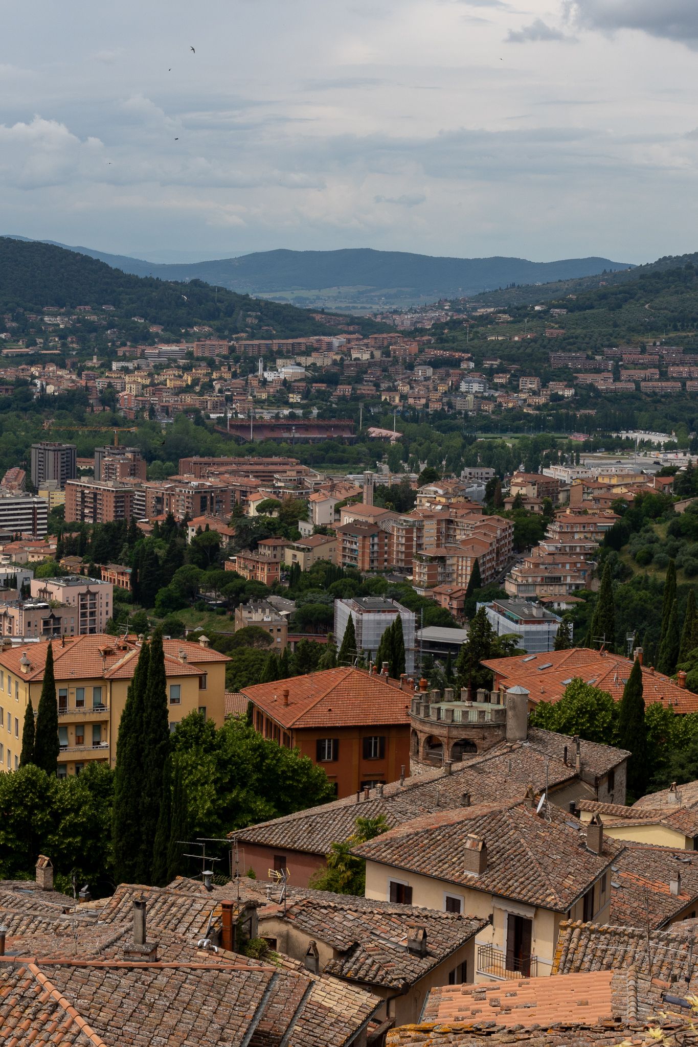 Aerial view of Italian hillside town with terra cotta roofs surrounded by mountains.