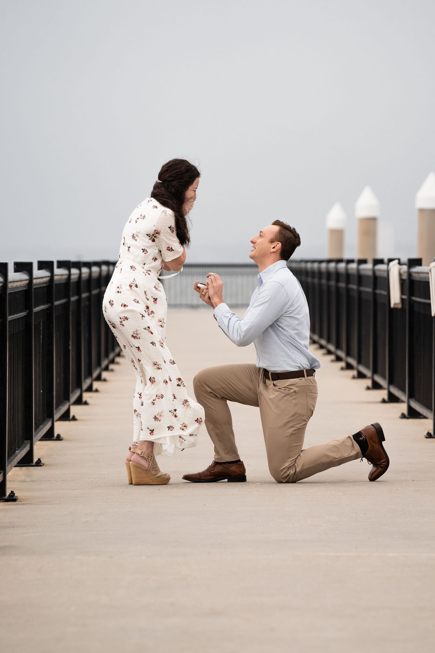 Romantic proposal scene on a pier with person kneeling.