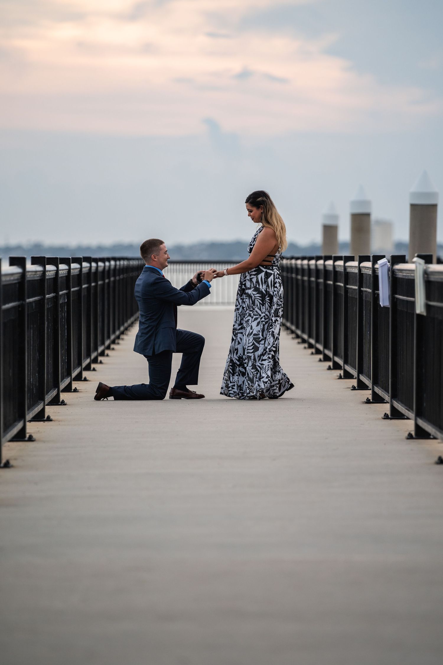 Marriage proposal moment on a waterfront pier during sunset.