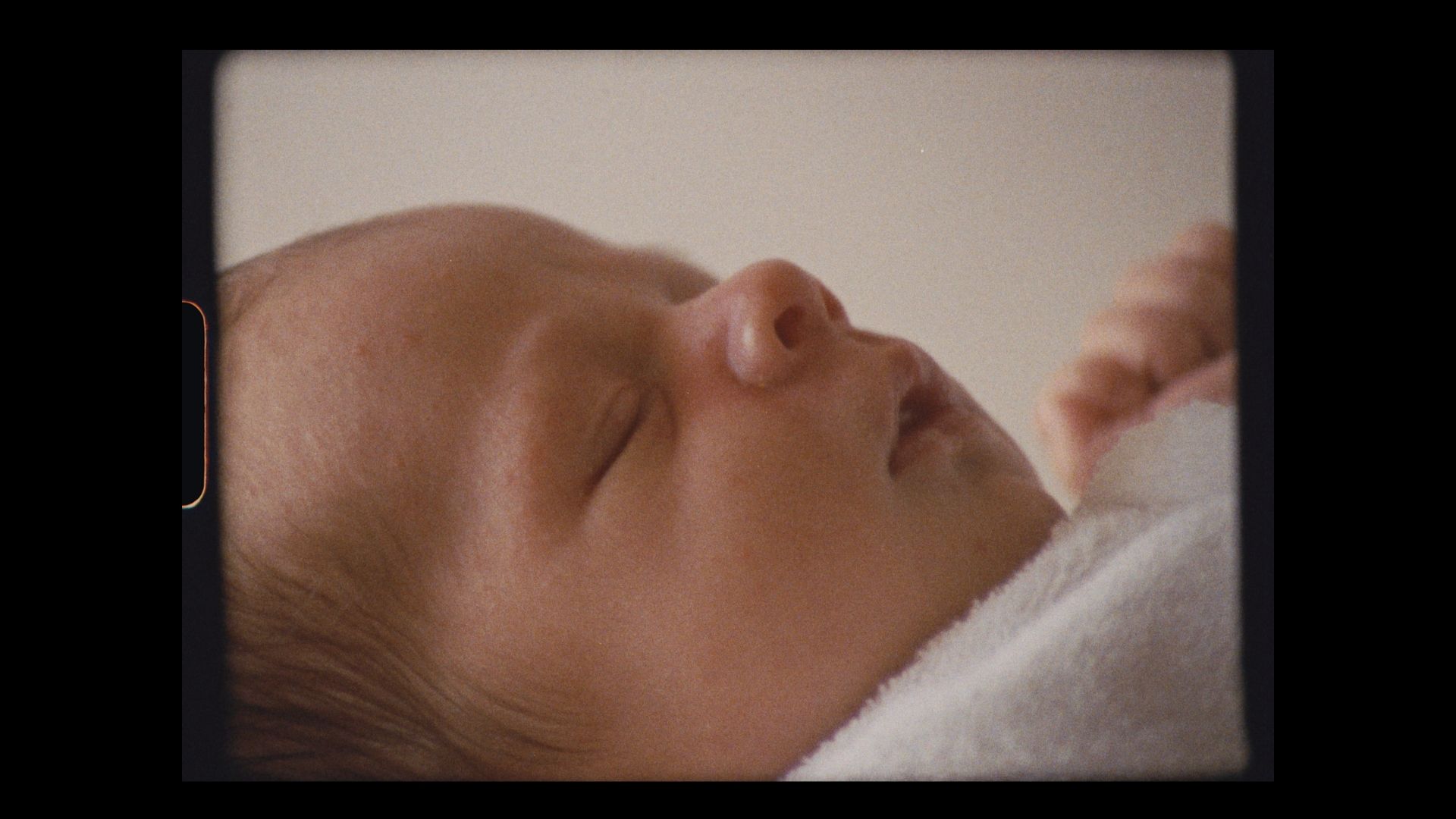 Close-up profile of a peaceful sleeping newborn baby against white fabric.