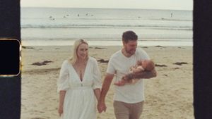 Family walking together on a beach in casual white clothing.