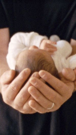 Gentle hands cradle a tiny newborn baby wrapped in soft white clothing.