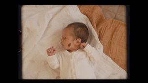 A sleeping newborn in white clothing lies on soft white bedding.