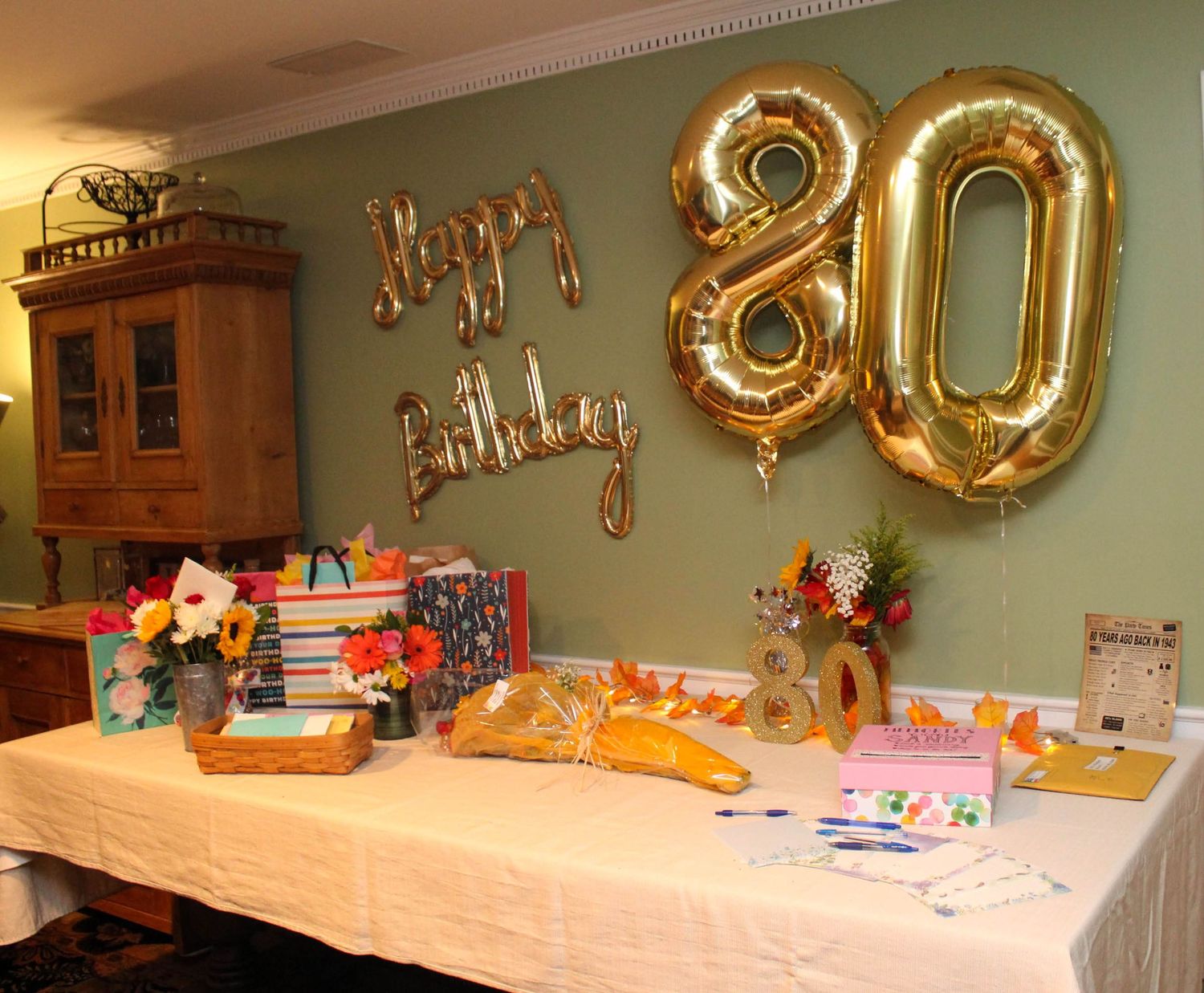 Birthday party table setup with gold number 80 balloons and presents.