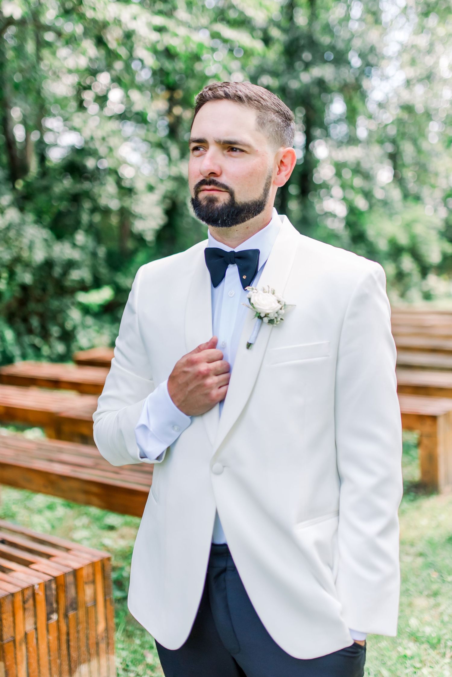 Groom in navy blue suit and burgundy bow tie adjusting cufflinks.