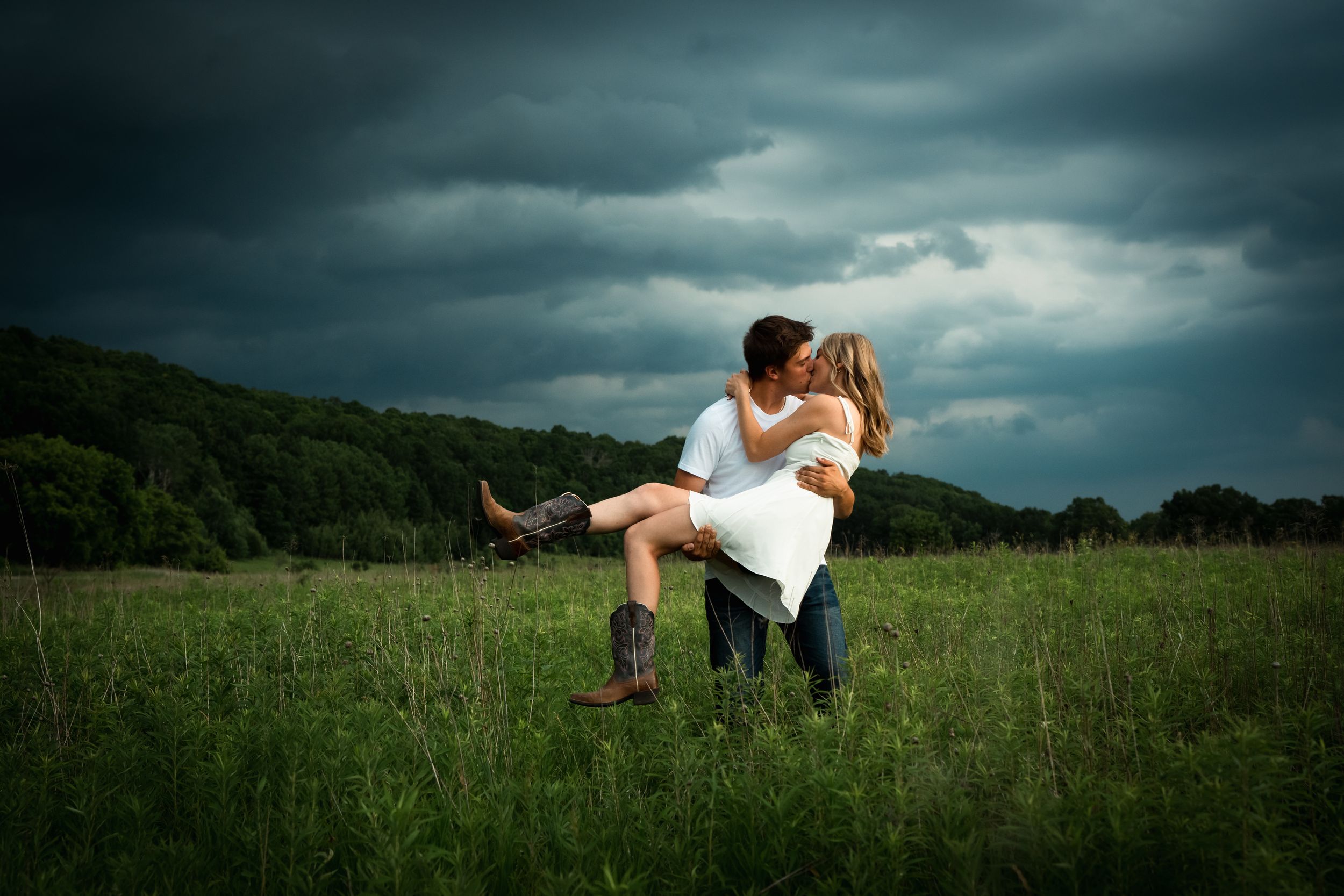 A romantic couple floats ethereally above a lush green meadow under dramatic stormy clouds.