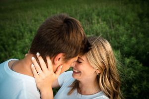 A couple in white shirts share an intimate laughing moment together in a green field.
