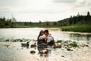 A romantic couple shares tender moments while wading in a serene lily-covered lake during sunset.