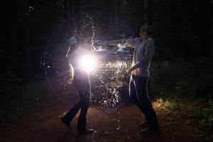Sparklers create magical light trails as figures dance in the dark forest at night.