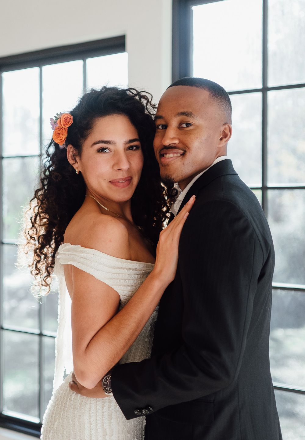 A bride and groom share intimate moments in a series of romantic poses by large windows in a modern setting.
