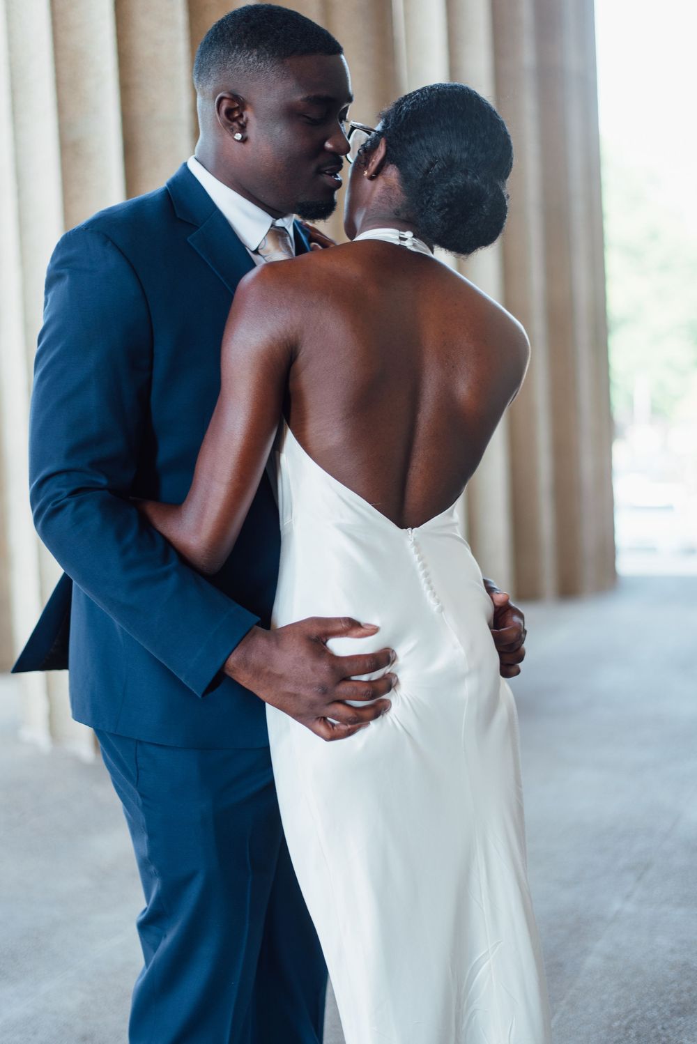 A couple shares an intimate dance moment at their wedding, with the bride in white and groom in navy blue suit.