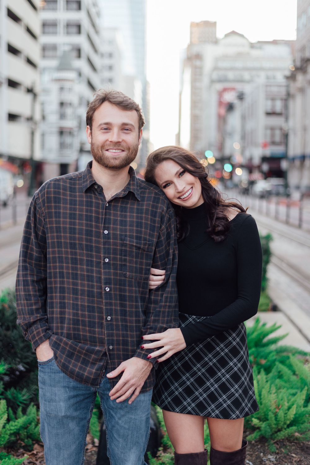 A happy couple poses together on a city street with tall buildings in the background on an overcast day.