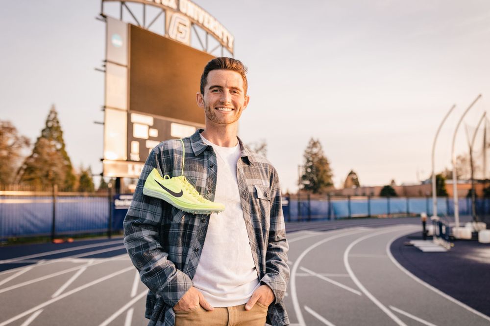 A person in plaid holds athletic shoes while standing on a blue running track at George Fox University.
