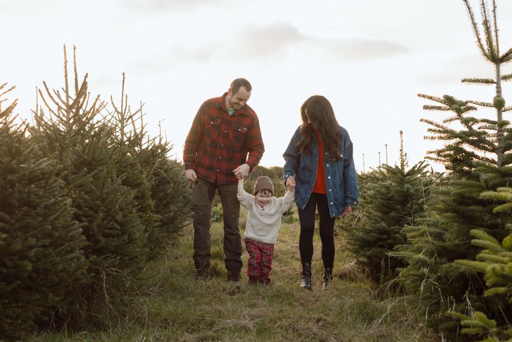 Mum, Dad and 2 year old boy walking through a Christmas tree farm smiling wearing earthy tones