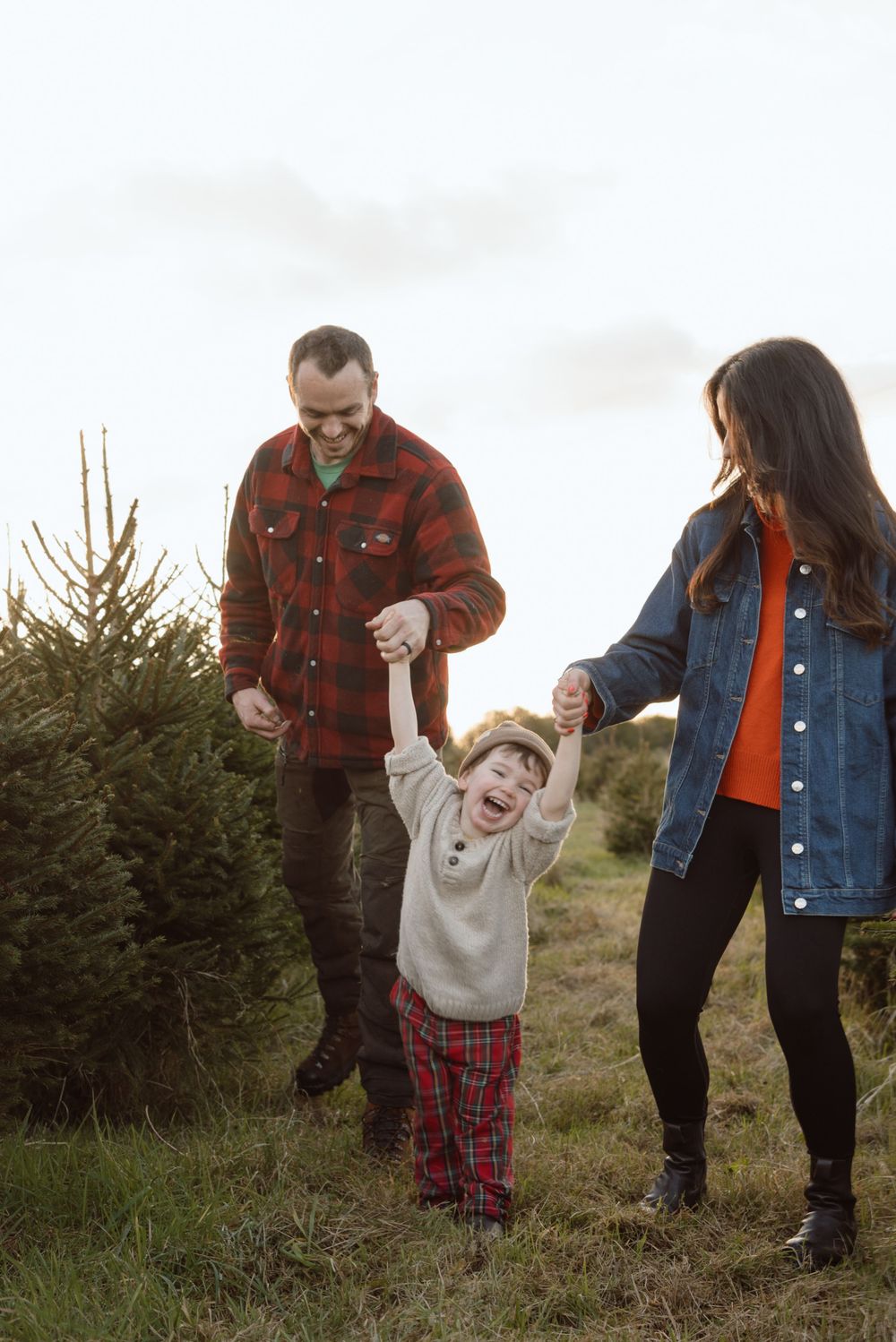 Dad & mum holding hands with son walking playfully through a christmas tree farm