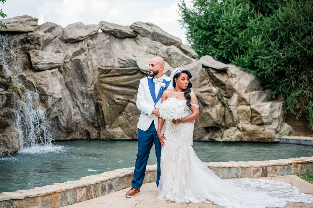 Newlyweds pose together in front of a picturesque rock waterfall at an outdoor wedding venue.